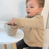 Kind hand reikt naar gezonde snack in Edessa Grabbel Snackkom met ergonomische handvaten en spiraalopening om morsen te voorkomen.