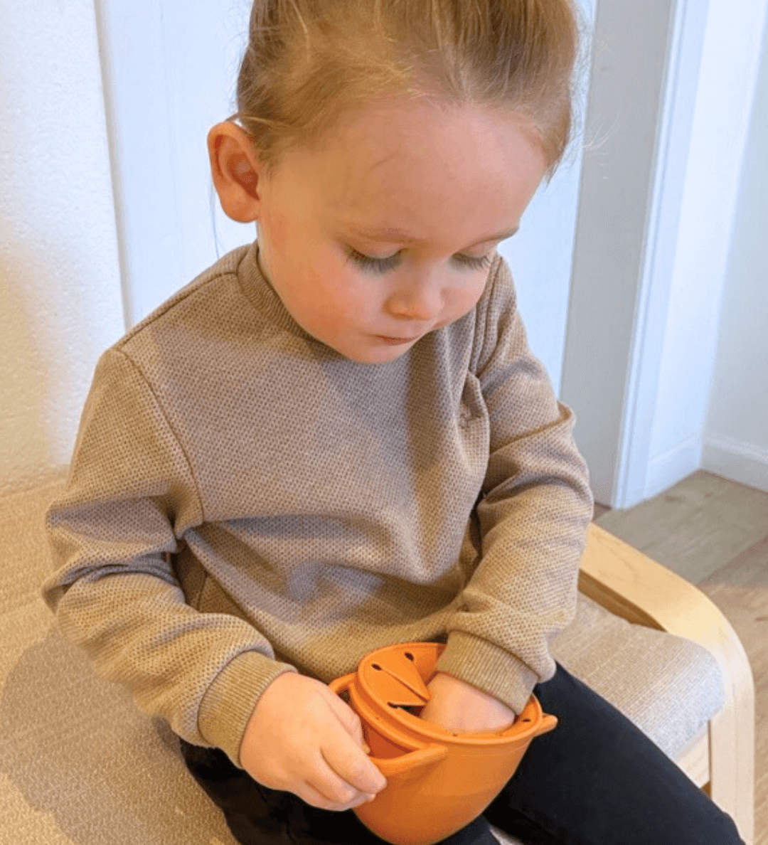 Kind hand reikt naar gezonde snack in Edessa Grabbel Snackkom met ergonomische handvaten en spiraalopening om morsen te voorkomen.