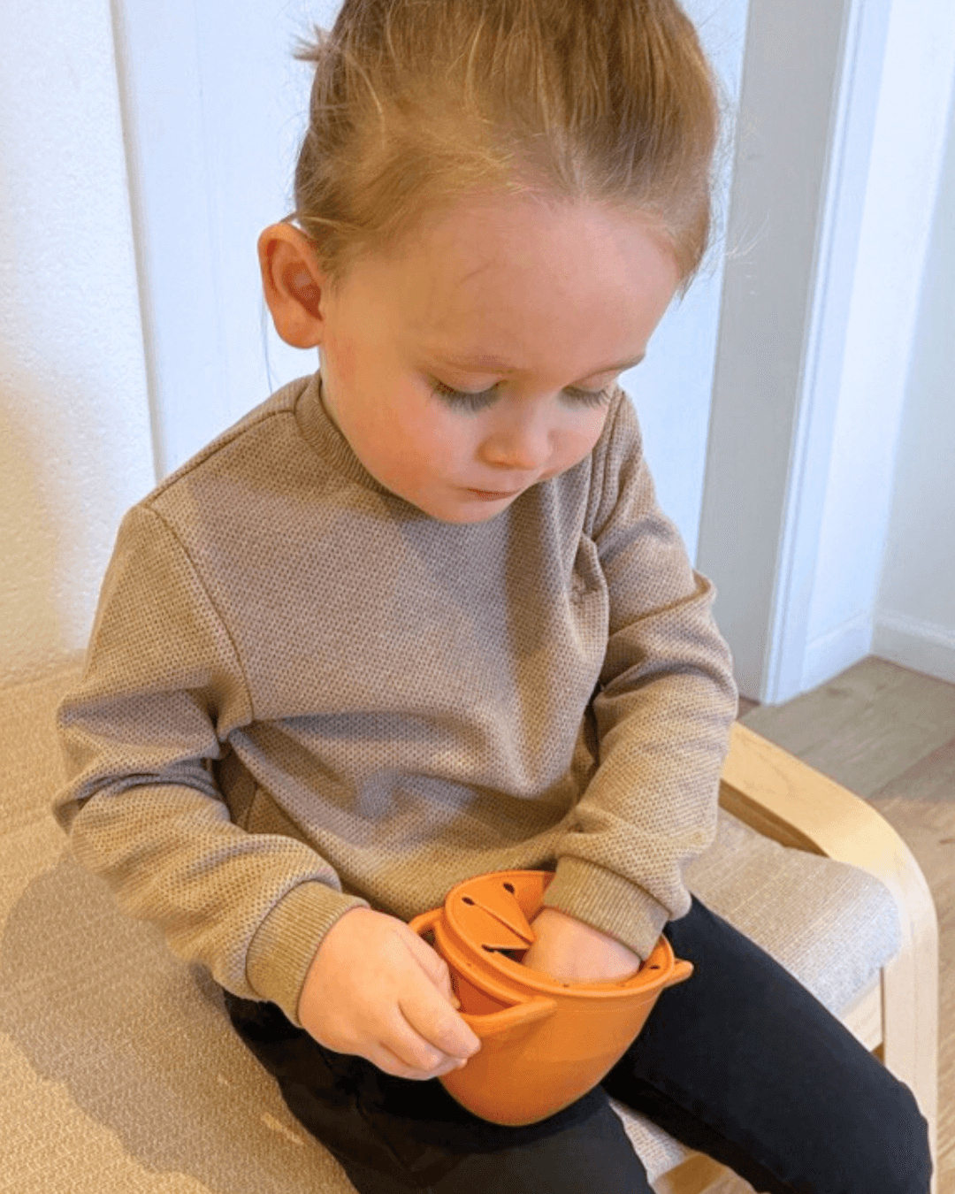 Kind hand reikt naar gezonde snack in Edessa Grabbel Snackkom met ergonomische handvaten en spiraalopening om morsen te voorkomen.